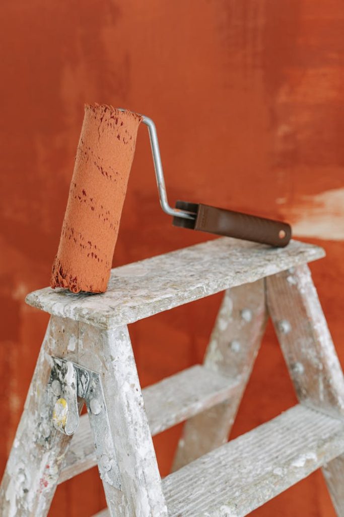 A paint roller rests on a stepladder against a painted wall, capturing a home renovation scene.